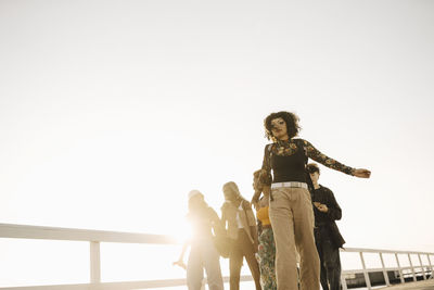 Teenage girl walking with friends on pier against clear sky