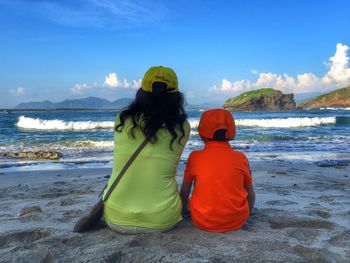 Rear view of mother with son sitting at beach against sky