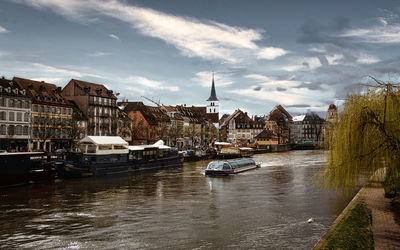 Sailboats moored on canal amidst buildings in city against sky