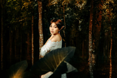 Portrait of woman sitting on tree trunk in forest