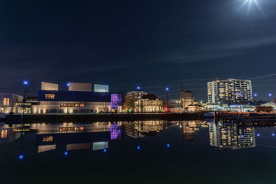 Illuminated buildings by river against sky at night