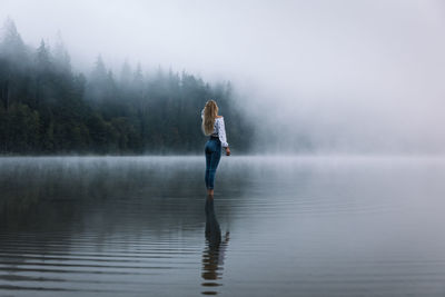 Young blonde fit woman standing in the foggy calm mirror lake and enjoying the nature in the forest.