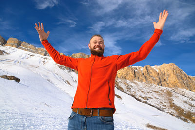 A bearded attractive caucasian man in a red sweater and jeans joyfully throws up his hands 