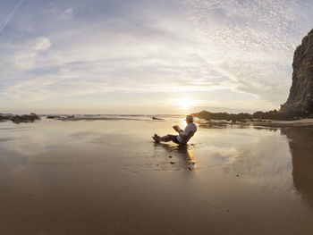 Portugal, senior man sitting at beach, reading book