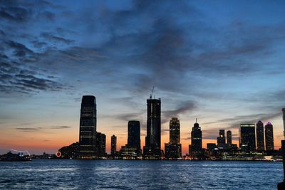 Sea by modern buildings against sky during sunset