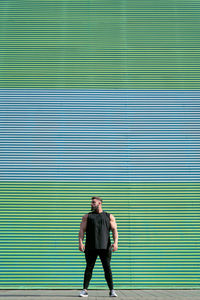 Full body of strong muscular male in sportswear standing on street near colorful wall on sunny street in city