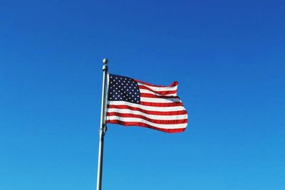 Low angle view of flag against clear blue sky