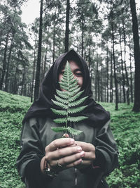 Close-up of young woman holding plant against her face in forest