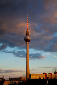 Communications tower in city against sky during sunset