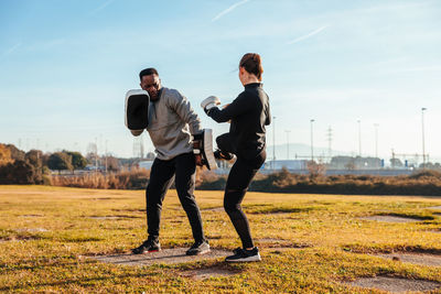 Full length of woman and man exercising on field against sky