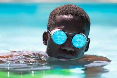 Calm african american male in stylish sunglasses with reflection of water swimming in pool against blurred background on sunny summer day