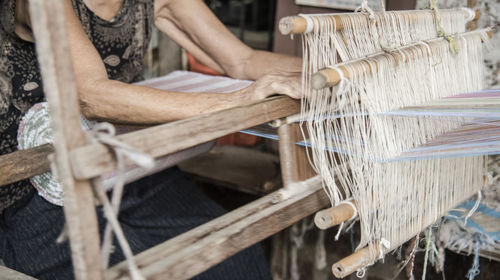 Midsection of woman weaving loom in factory