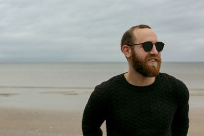 Young man standing at beach against sky