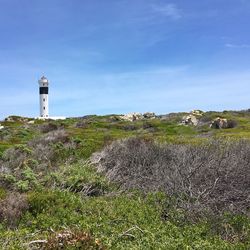 Lighthouse on landscape against blue sky