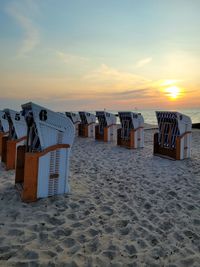 Hooded chairs on beach against sky during sunset