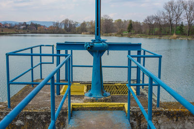 Metal railing by lake against sky