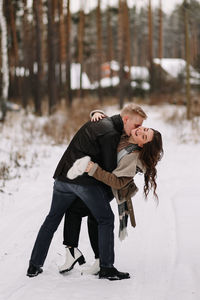 A happy couple in love in winter clothes hugging together walking in a snowy forest on an weekend