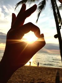 Close-up of silhouette hand against sea during sunset