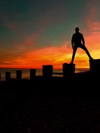 Silhouette man standing on beach against sky during sunset