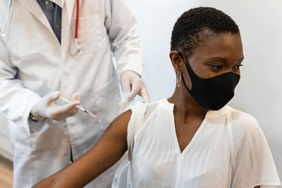Crop male medic making injection for black female patient in mask