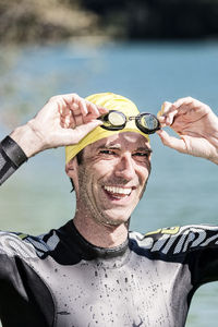 Portrait of happy male triathlete removing goggles while standing against river