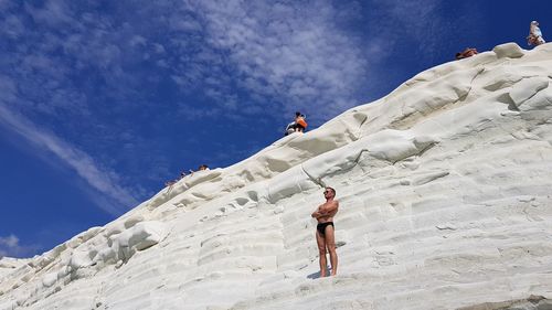 Low angle view of man climbing on mountain against sky