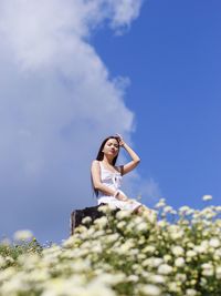 Low angle view of young woman sitting against sky