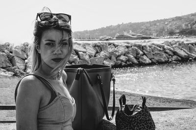 Close-up portrait of woman with purses on retaining wall against sea