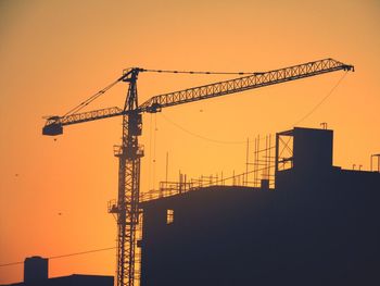 Silhouette cranes at construction site against sky during sunset