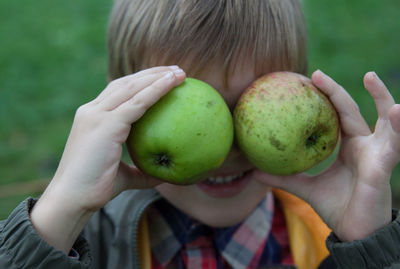 Close-up boy holding apples on his eyes