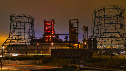 Illuminated factory against sky at night