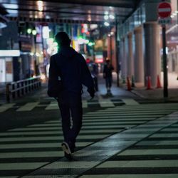 Rear view of man walking on pedestrian crossing in city