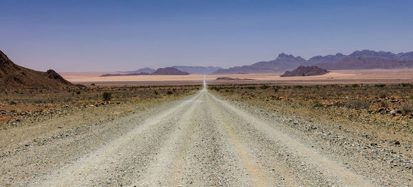 Dirt road amidst desert against sky