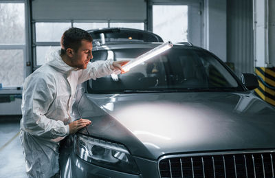 Illuminating the car surface. man in uniform is working in the auto service.