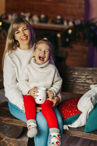 Portrait of a happy little girl sitting on her mother's lap and drinking hot chocolate on christmas