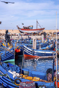 Wooden blue fishing boats anchored at marina against cloudy sky