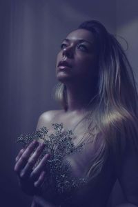 Close-up of thoughtful shirtless woman holding plant against wall