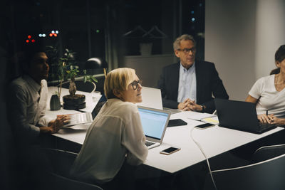 Male and female entrepreneurs sitting in board room during conference call at late night in office