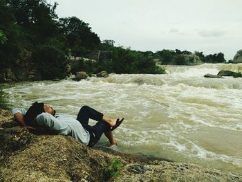 Man relaxing at riverbank against sky