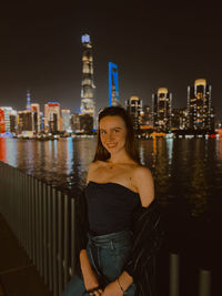 Portrait of smiling woman against illuminated buildings in city at night