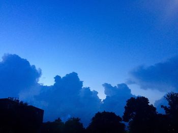Low angle view of silhouette trees against blue sky