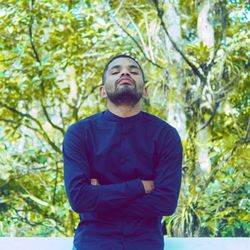 Young man looking away against trees