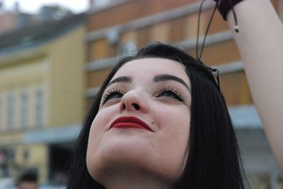 Close-up of smiling young woman looking up while standing in city