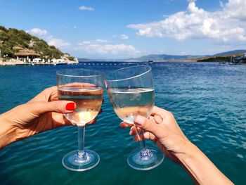 Cropped hands celebrating toast against sea