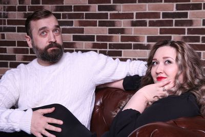 Thoughtful couple sitting on sofa against brick wall