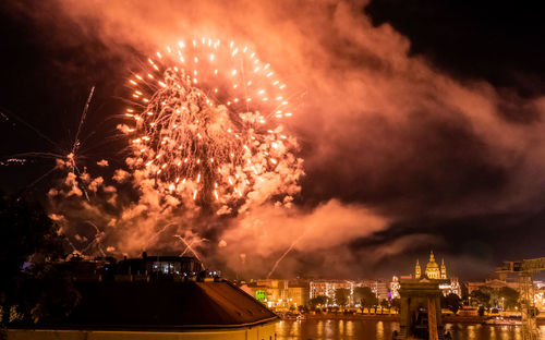 Firework display over illuminated city against sky at night