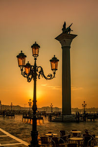 Silhouette street light by sea against orange sky