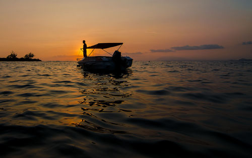 Silhouette person standing in boat on sea against sky during sunset