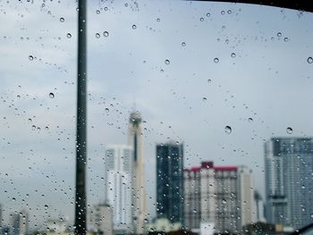 Close-up of wet glass window against sky