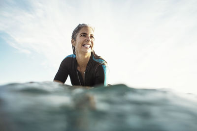 Surface level of happy wet woman surfing on sea against sky